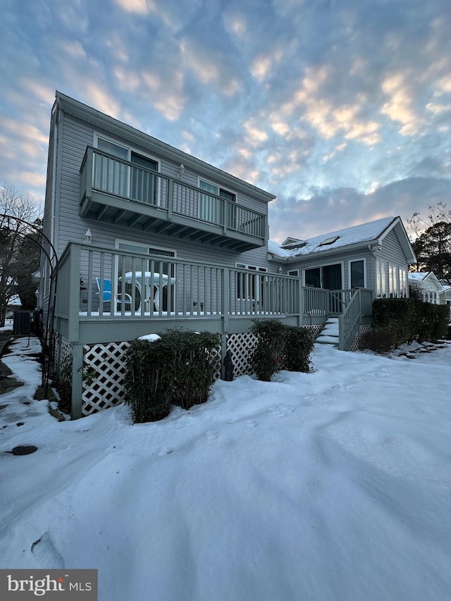 snow covered property with a balcony and a wooden deck