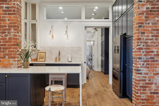 bar with light wood-type flooring, refrigerator, light stone counters, decorative backsplash, and sink