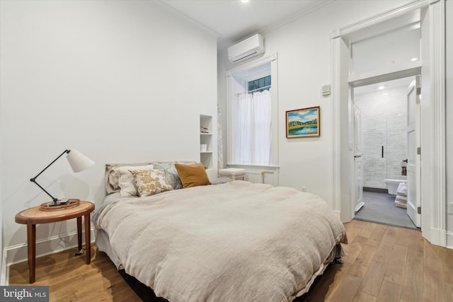 bedroom with a wall mounted air conditioner, ensuite bathroom, ornamental molding, and hardwood / wood-style flooring