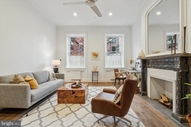 sitting room featuring a high end fireplace, light wood-type flooring, ceiling fan, and crown molding