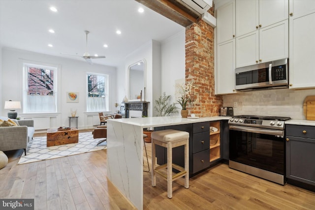 kitchen featuring light wood-type flooring, tasteful backsplash, kitchen peninsula, and appliances with stainless steel finishes