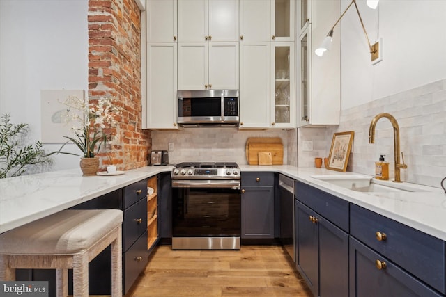 kitchen with appliances with stainless steel finishes, light stone counters, decorative backsplash, white cabinets, and sink