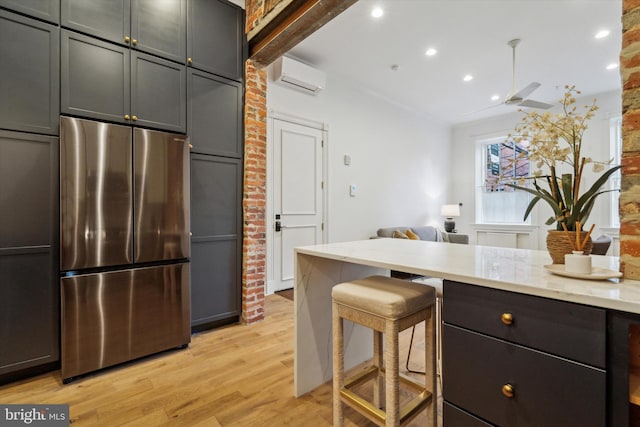 kitchen featuring light wood-type flooring, beam ceiling, stainless steel refrigerator, a wall mounted air conditioner, and a kitchen breakfast bar