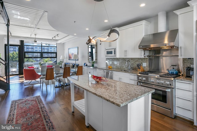 kitchen featuring stainless steel appliances, decorative light fixtures, white cabinets, wall chimney exhaust hood, and decorative backsplash