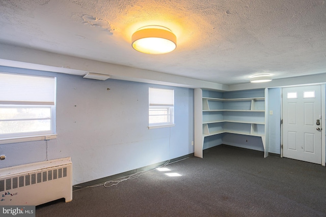 basement with plenty of natural light, radiator, a textured ceiling, and dark colored carpet