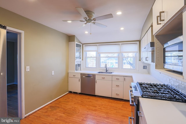 kitchen featuring appliances with stainless steel finishes, sink, white cabinets, wall chimney exhaust hood, and light hardwood / wood-style flooring