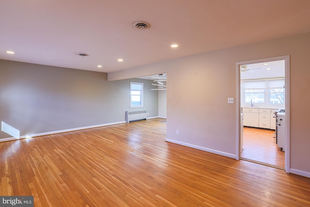 spare room featuring radiator, sink, and light hardwood / wood-style flooring