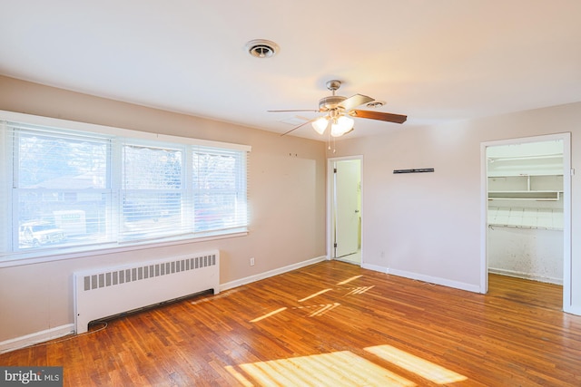 unfurnished bedroom with radiator, ceiling fan, wood-type flooring, a walk in closet, and a closet