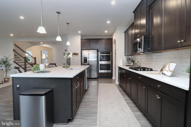 kitchen featuring pendant lighting, tasteful backsplash, sink, stainless steel appliances, and a center island with sink