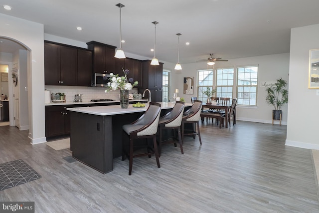 kitchen with dark brown cabinetry, decorative light fixtures, a center island with sink, and backsplash