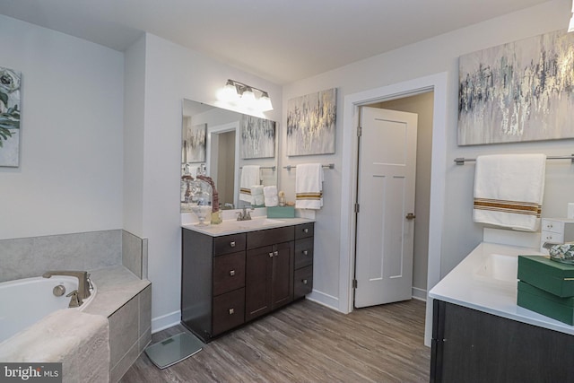 bathroom with hardwood / wood-style flooring, vanity, and a relaxing tiled tub