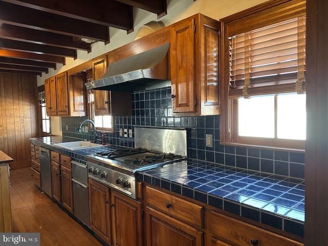 kitchen featuring tile countertops, backsplash, a sink, and beamed ceiling