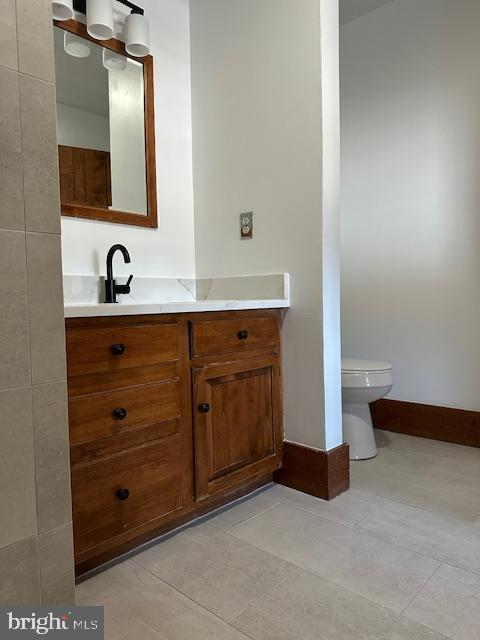 bathroom with toilet, tile patterned floors, baseboards, and vanity