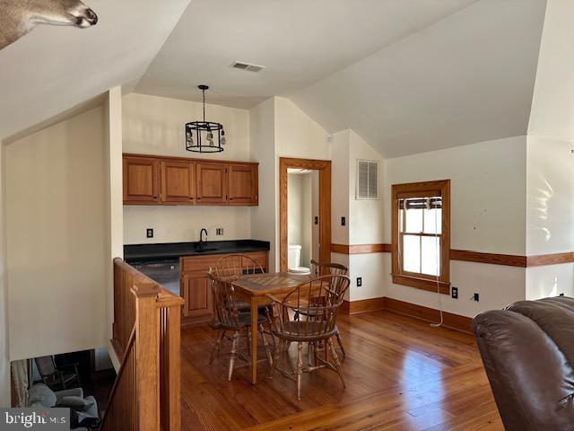 kitchen featuring wood finished floors, visible vents, dishwasher, brown cabinetry, and dark countertops