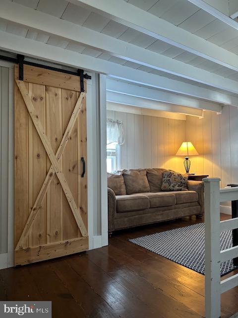 living room featuring a barn door, dark wood finished floors, and beam ceiling