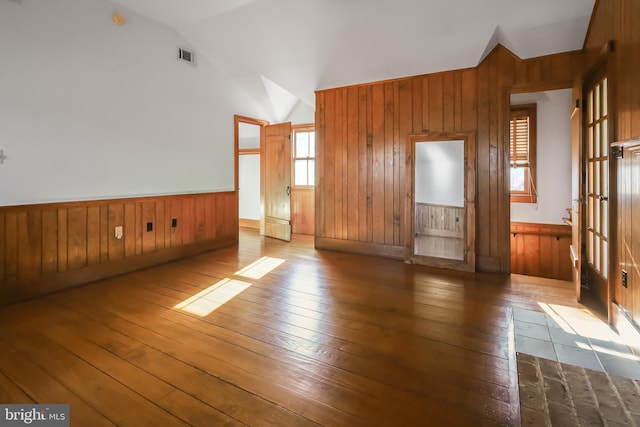 unfurnished living room with wood-type flooring, wainscoting, vaulted ceiling, and wooden walls