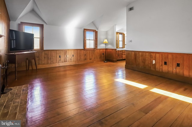 unfurnished living room featuring hardwood / wood-style flooring, visible vents, vaulted ceiling, and wainscoting