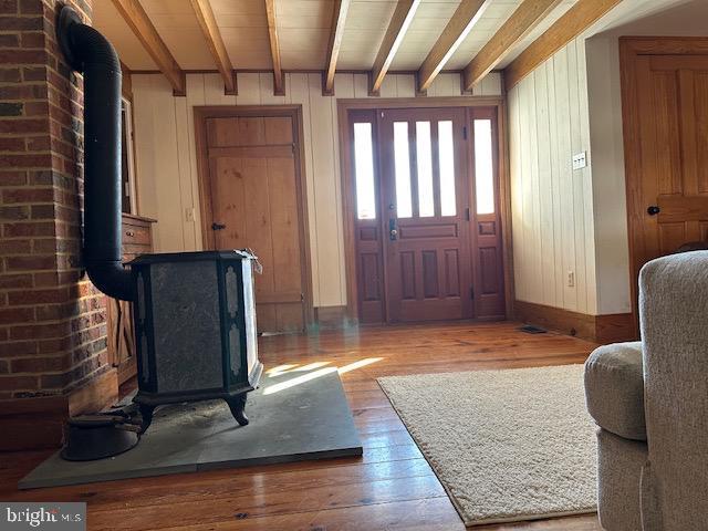 foyer featuring hardwood / wood-style flooring, wood walls, baseboards, beamed ceiling, and a wood stove