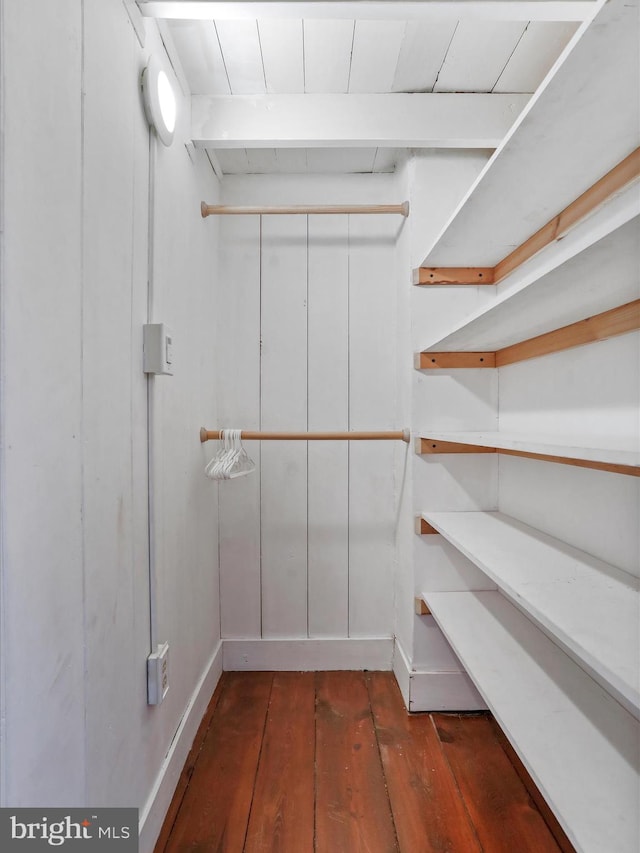 spacious closet with dark wood-style flooring and beamed ceiling