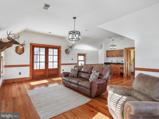 living area featuring french doors, light wood finished floors, lofted ceiling, visible vents, and baseboards