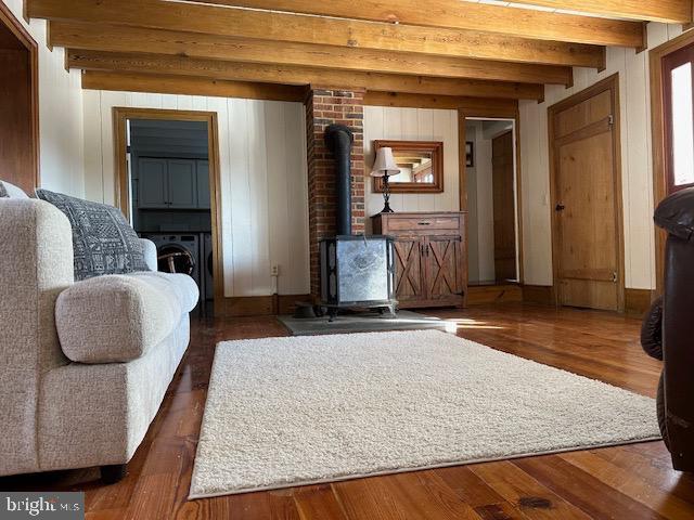 unfurnished living room featuring a wood stove, beam ceiling, and wood finished floors