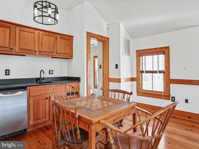 kitchen featuring dark countertops, light wood-style flooring, vaulted ceiling, a sink, and dishwasher