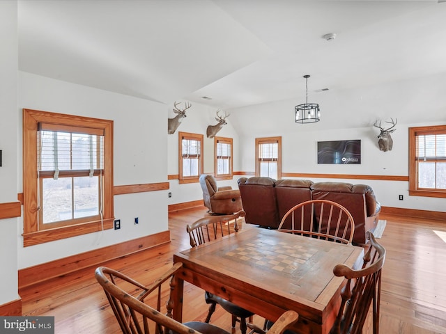 dining space with a notable chandelier, baseboards, lofted ceiling, and light wood-style floors