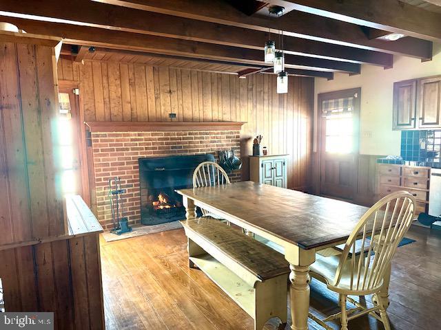 dining room with ceiling fan, hardwood / wood-style flooring, wood walls, a fireplace, and beam ceiling