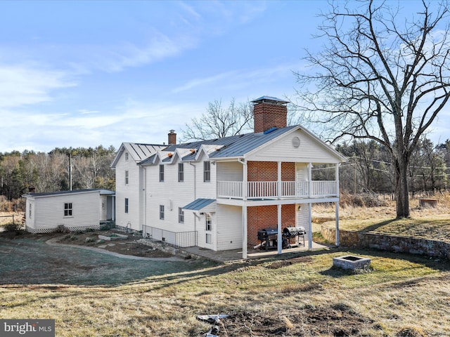 rear view of property featuring a yard, a chimney, a standing seam roof, metal roof, and a fire pit