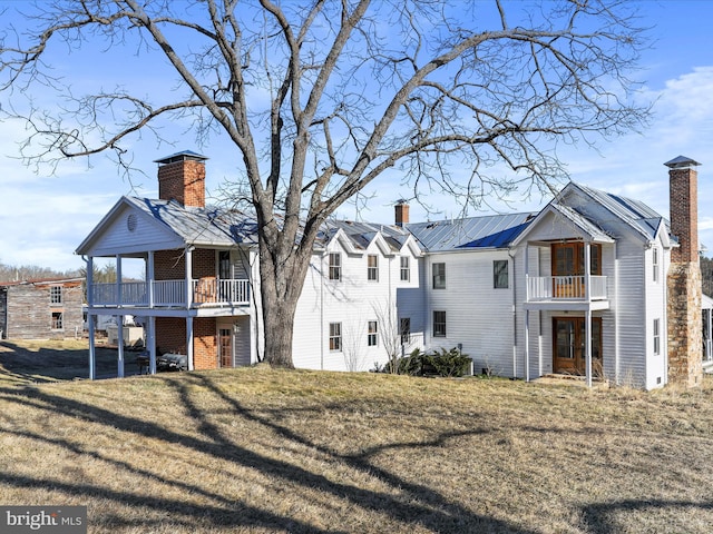 rear view of house with metal roof, a yard, a chimney, and a standing seam roof