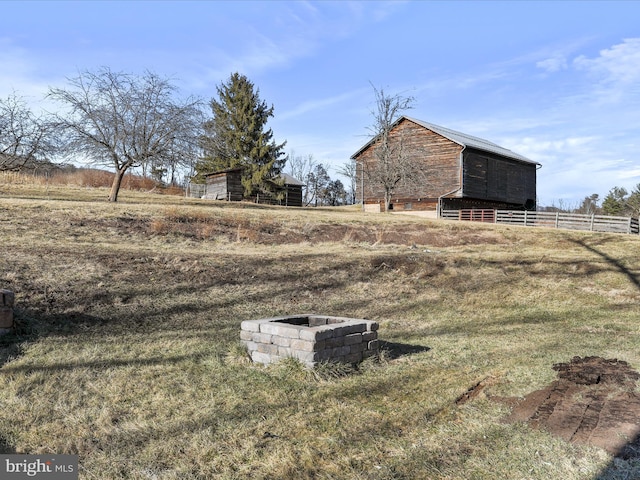 view of yard with an outbuilding, an outdoor fire pit, fence, a barn, and a rural view