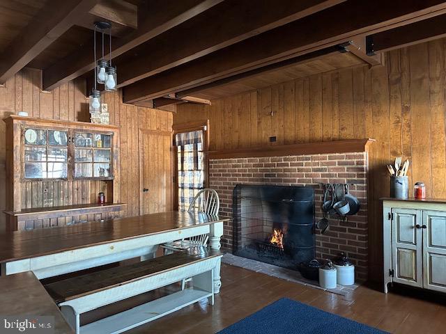 interior space with wood walls, a brick fireplace, beam ceiling, and wood finished floors