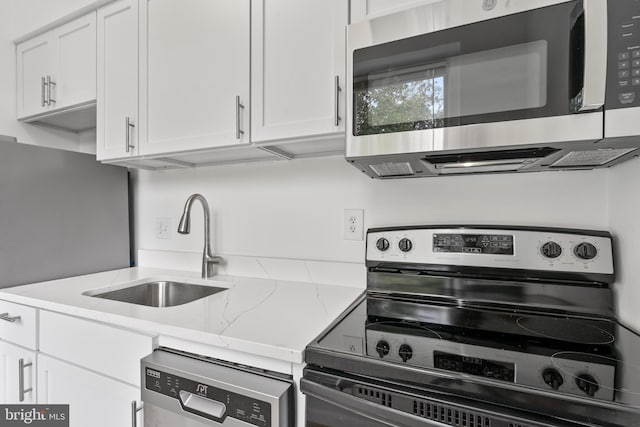 kitchen featuring light stone counters, white cabinets, appliances with stainless steel finishes, and sink