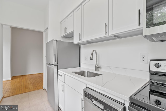 kitchen featuring light stone countertops, light tile patterned floors, white cabinets, appliances with stainless steel finishes, and sink