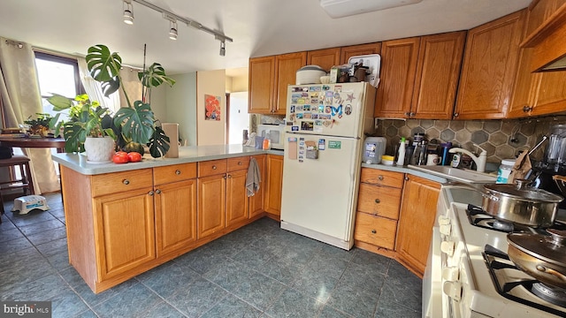 kitchen with kitchen peninsula, decorative backsplash, white appliances, track lighting, and sink