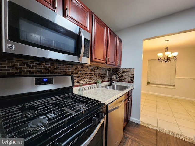 kitchen with stainless steel appliances, sink, decorative light fixtures, dark tile patterned floors, and a notable chandelier