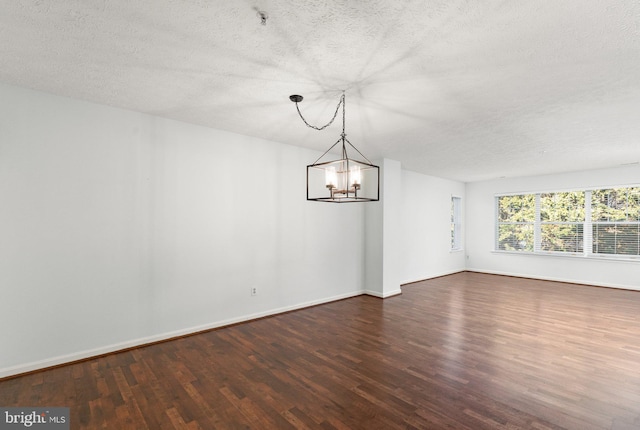 empty room with dark hardwood / wood-style flooring, an inviting chandelier, and a textured ceiling