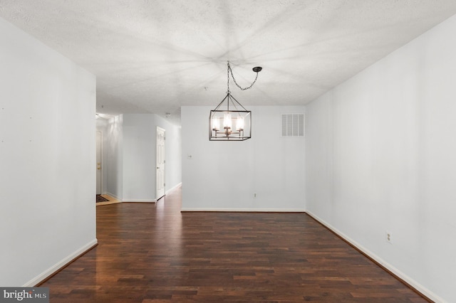 unfurnished dining area featuring an inviting chandelier, a textured ceiling, and dark hardwood / wood-style flooring