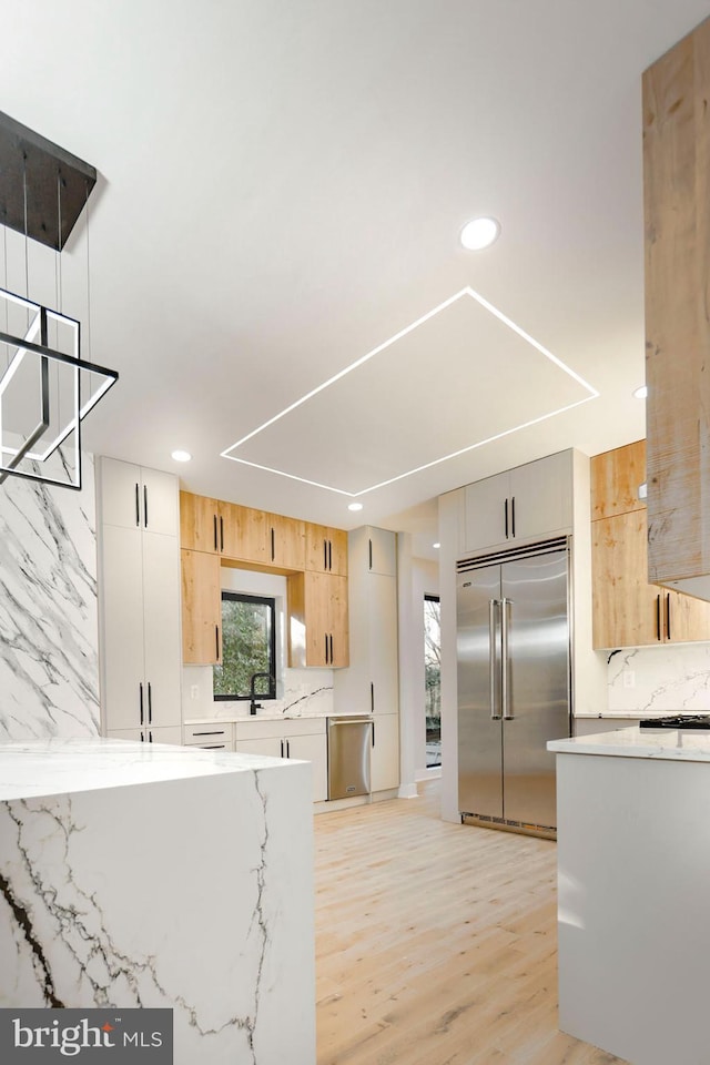 kitchen with stainless steel appliances, light stone counters, light hardwood / wood-style floors, light brown cabinetry, and decorative backsplash