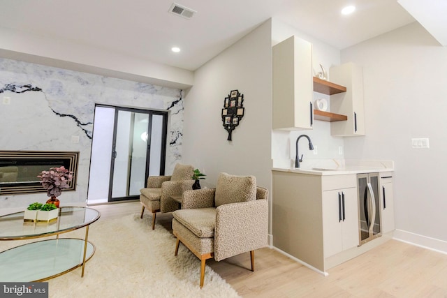 living room with wine cooler, a high end fireplace, sink, and light wood-type flooring