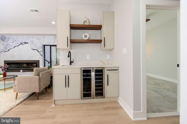 bar featuring wine cooler, sink, white cabinetry, light hardwood / wood-style flooring, and a high end fireplace