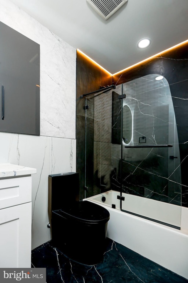 full bathroom featuring toilet, vanity, bath / shower combo with glass door, and tile walls