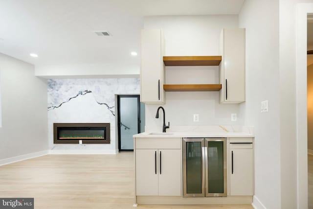 kitchen featuring wine cooler, sink, white cabinetry, light hardwood / wood-style flooring, and a premium fireplace