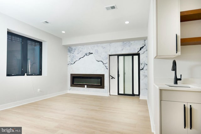 unfurnished living room with sink, a high end fireplace, and light wood-type flooring