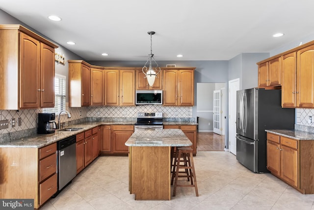 kitchen with sink, stainless steel appliances, a center island, stone countertops, and decorative light fixtures