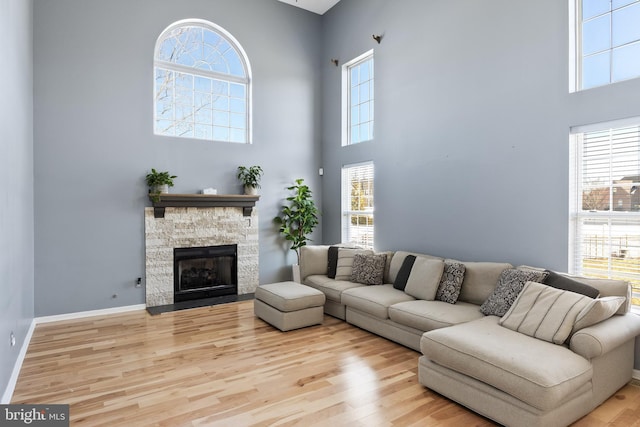 living room featuring light wood-type flooring, a fireplace, and a towering ceiling