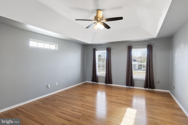 empty room featuring ceiling fan, a tray ceiling, and light wood-type flooring