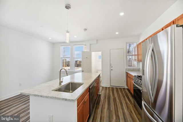 kitchen with light stone counters, pendant lighting, a center island with sink, appliances with stainless steel finishes, and sink