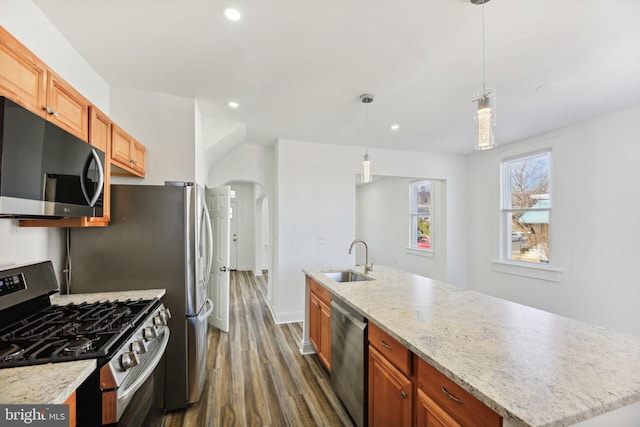 kitchen featuring dark wood-type flooring, decorative light fixtures, a kitchen island with sink, appliances with stainless steel finishes, and sink