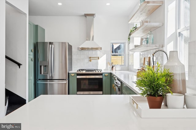 kitchen featuring green cabinetry, stainless steel appliances, decorative backsplash, and wall chimney range hood